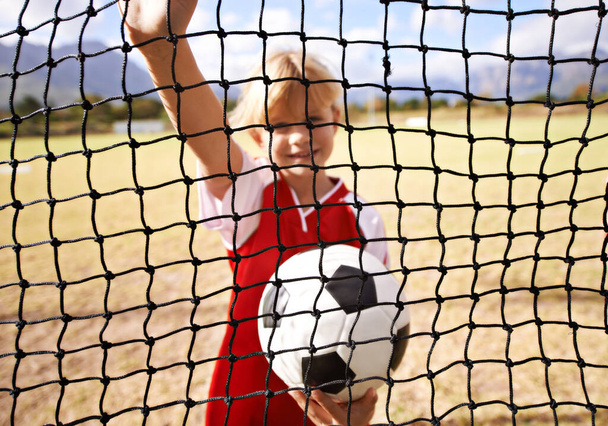 This is where the ball will end up. Portrait of a young girl standing behind the net on a soccer field - Foto, afbeelding