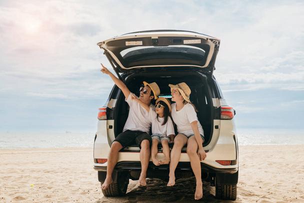 Happy Family Day. Family travel in holiday at sea beach, Dad, mom, daughter enjoy road trip sitting on back car and pointing finger out, people having fun in summer vacation on beach with automobile - Foto, imagen