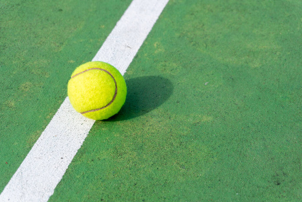 Tophoek uitzicht op tennisbal op het veld. Gele tennisbal op groene baan en witte lijnen. - Foto, afbeelding