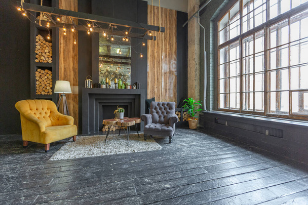 dark brutal interior of sitting room decorated with wooden logs. yellow and grey soft armchairs, huge arc window and fireplace - Фото, зображення