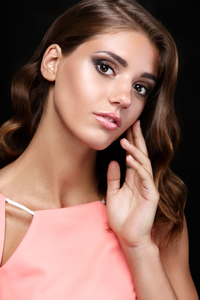 Beautiful woman in a pink romantic dress with smooth wavy hair and smoky eyes make up  on black background - Foto, imagen
