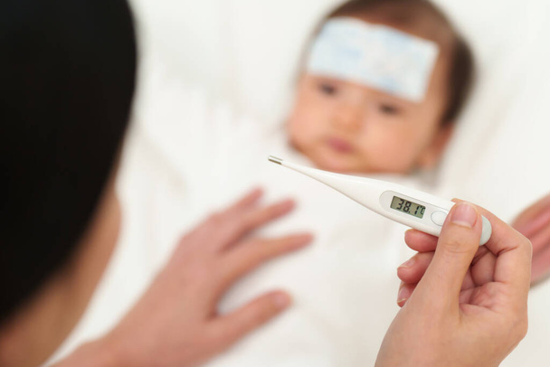 mother measuring temperature of her sick baby with cool fever jel pad. displey high fever temperature - 写真・画像