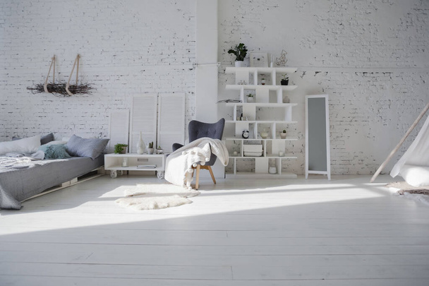 Spacious stylish modern trendy loft apartment in white and light colors. a large room full of sunlight. brick wall, wood floor, shelving, pallet bed and huge window. everything is white with gray tints. - Foto, afbeelding
