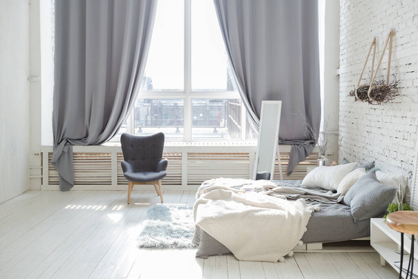 Spacious stylish modern trendy loft apartment in white and light colors. a large room full of sunlight. brick wall, wood floor, shelving, pallet bed and huge window. everything is white with gray tints. - Valokuva, kuva