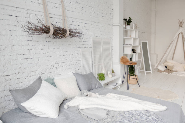Spacious stylish modern trendy loft apartment in white and light colors. a large room full of sunlight. brick wall, wood floor, shelving, pallet bed and teepee-shaped children's house. everything is white with gray tints. - Fotoğraf, Görsel