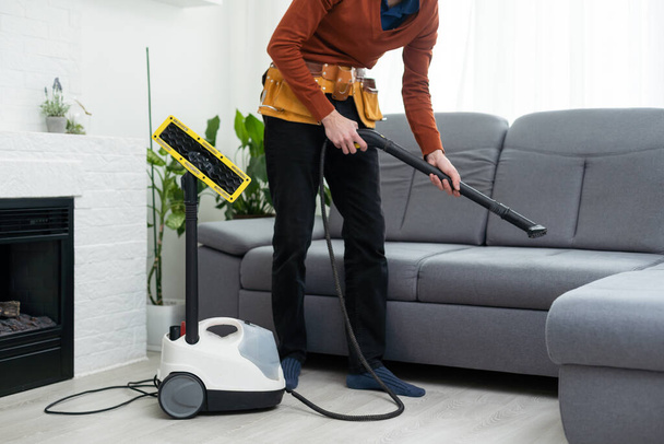 Dry cleaners man employee removing dirt from furniture in flat, closeup, vacuum clean sofa with professional equipment - Foto, imagen