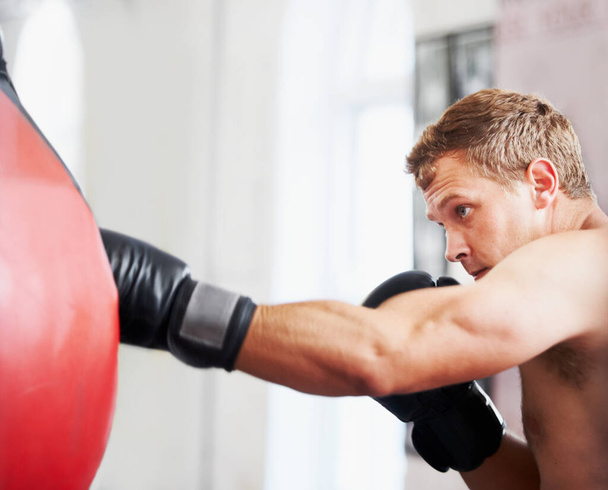 Strength and focus. A young boxer practicing with a punching ball - Фото, зображення