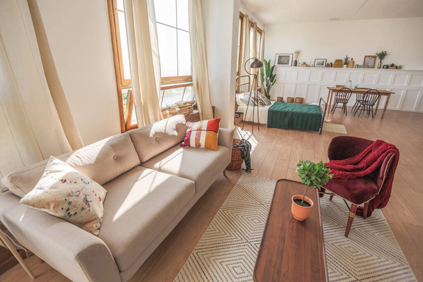 Vintage studio apartment interior in light colors in old style. huge room with large windows with a living room area and a bedroom area. direct sunlight inside. - Photo, image