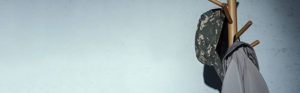Vojenská čepice s maskovacím vzorem zavěšeným na podlahovém ramínku doma, prapor  - Fotografie, Obrázek