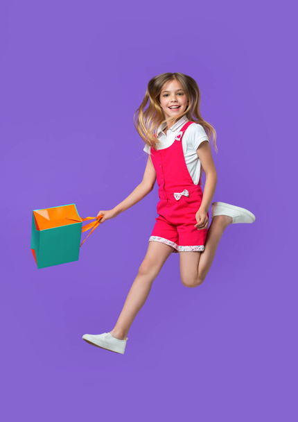 image of teen girl jumping after shopping. teen girl jumping after shopping isolated on purple. teen girl jumping after shopping in studio. teen girl jumping after shopping on background. - Photo, image