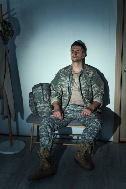 Μοναχικός βετεράνος του στρατού με μετατραυματική διαταραχή άγχους που κάθεται στο διάδρομο στο σπίτι τη νύχτα  - Φωτογραφία, εικόνα