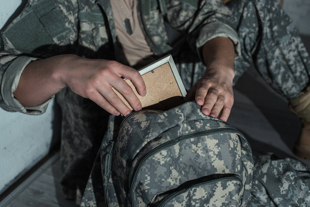 Gehakt beeld van soldaat met psychische problemen het nemen van fotolijst uit rugzak thuis 's nachts  - Foto, afbeelding