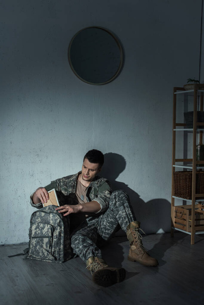 Soldat avec destresse mentale prenant le cadre photo du sac à dos à la maison la nuit  - Photo, image