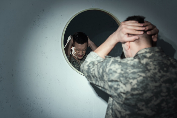 Stressed military veteran suffering from post traumatic stress disorder near mirror at home at night  - Photo, Image