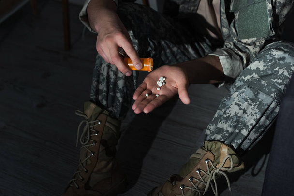 Oříznutý pohled na vojenského veterána nalévání pilulek po ruce, zatímco trpí emocionální úzkost doma v noci - Fotografie, Obrázek
