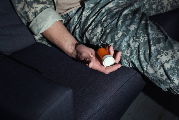 Vista recortada del soldado con ptsd sosteniendo pastillas en el sofá en casa - Foto, imagen