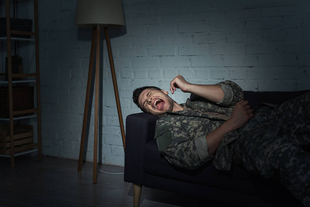 Stressed military man screaming while suffering from post traumatic stress disorder at home at night - Photo, Image