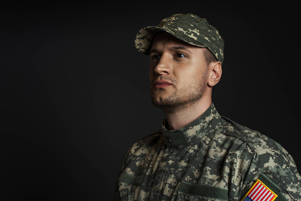 patriotický voják v uniformě s americkou vlajkou dívá pryč izolované na černé  - Fotografie, Obrázek