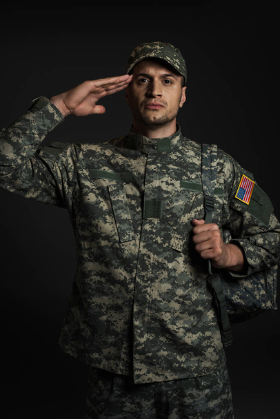 patriotic soldier in uniform with American flag saluting isolated on black  - Φωτογραφία, εικόνα