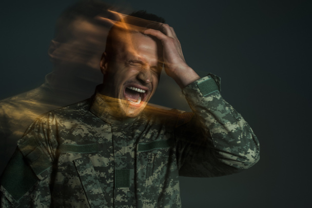 desenfoque de movimiento del soldado en uniforme de camuflaje gritando mientras sufre de ptsd aislado en gris oscuro  - Foto, imagen