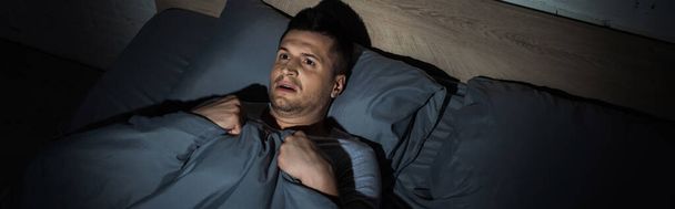 felső nézet rémült férfi szenved pánikroham és álmatlanság, miközben feküdt a takaró alatt, banner  - Fotó, kép