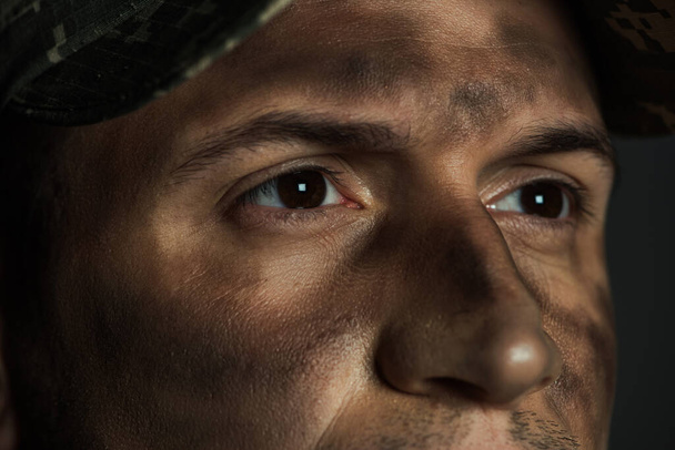 zblízka pohled na oči vojenského muže se špínou na tváři trpí ptsd izolované na šedé  - Fotografie, Obrázek