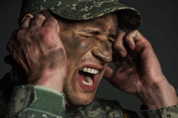 military man with dirt on face screaming while suffering from post traumatic stress disorder isolated on grey  - 写真・画像