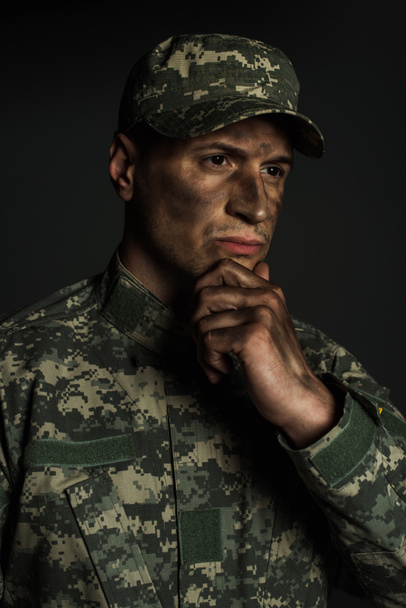 вдумчивый военнослужащий, касающийся подбородка грязной рукой, глядя в сторону, изолированную от серого  - Фото, изображение