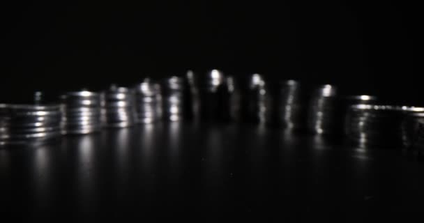 Kudrnaté řady komínů ze stříbrných mincí stojící na černém povrchu v tmavém ateliéru se slabým světlem. Koncepce peněžních investic a akumulace. Finanční úspory - Záběry, video