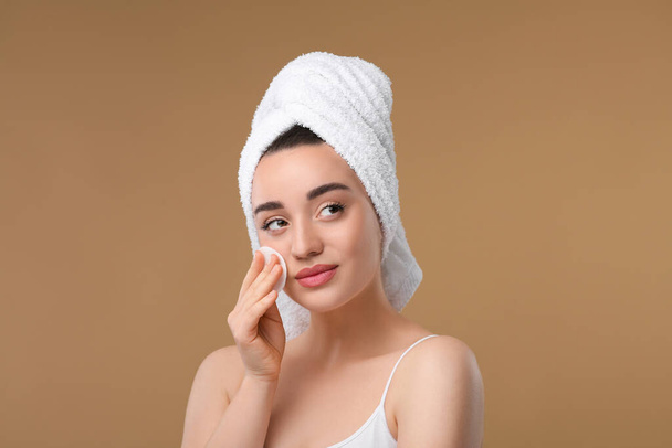 Beautiful woman in terry towel removing makeup with cotton pad on beige background - Fotografie, Obrázek