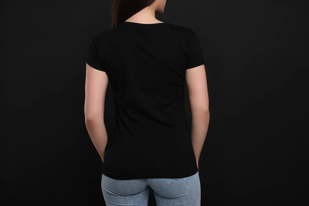Mujer con camiseta negra sobre fondo oscuro, vista trasera - Foto, imagen