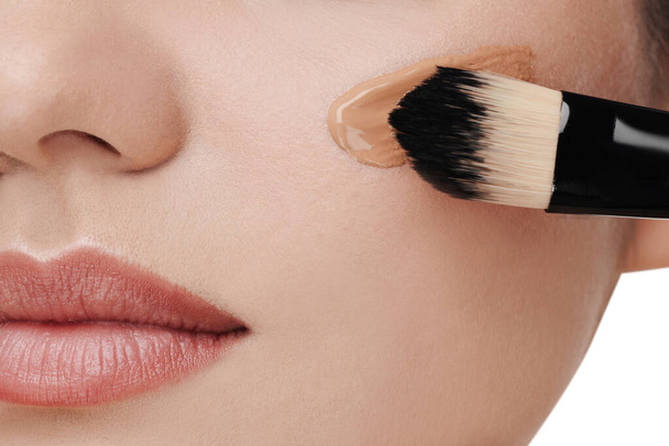 Woman applying foundation on face with brush against white background, closeup - Fotó, kép