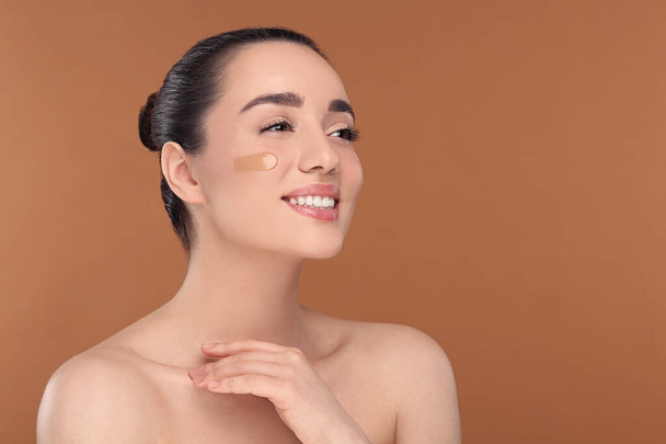 Woman with swatch of foundation on face against brown background. Space for text - Photo, Image