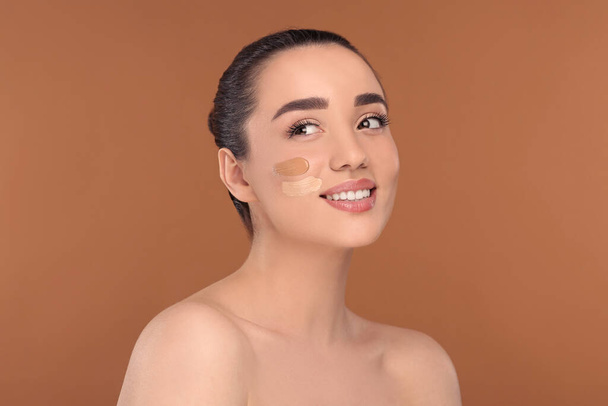 Woman with swatches of foundation on face against brown background - Foto, imagen