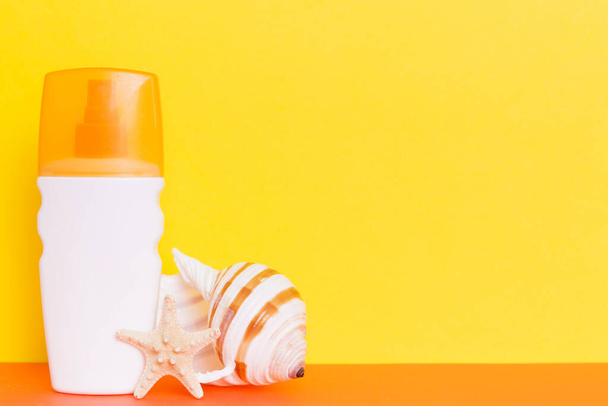 Beach accessories. Moisturiser sunscreen suntan lotion bottle for UVB skincare protection in summer with seashells on colored background. Mock up with copy space. - Photo, image