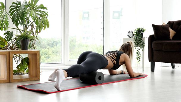 Adult athletic woman performing exercises on the floor - caucasian woman using a massage foam roller. - Фото, зображення