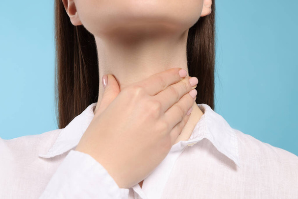 Woman with sore throat on light blue background, closeup - 写真・画像