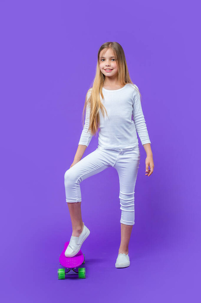 teen girl skateboarder in studio. teen girl skateboarder on background. image of teen girl skateboarder. teen girl skateboarder isolated on purple. - Foto, Imagem