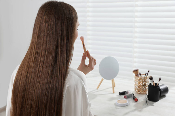 Woman applying makeup with brush at dressing table indoors. Space for text - Foto, immagini