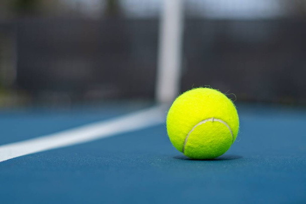 A closeup of a tennis ball on the court on a sunny day with a blurry background - Foto, Imagem