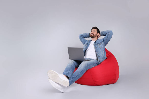 Happy man with laptop sitting on beanbag chair against light grey background - Φωτογραφία, εικόνα