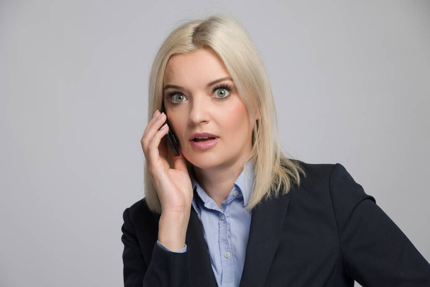 young blonde woman in business dress is using a cell phone and is listening - Foto, imagen