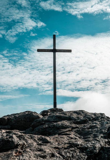 A vertical shot of the cross on the top of the stony hill against a blue sky - Foto, Imagen