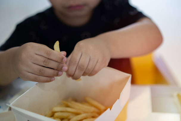 Crianças mãos Picking French Fries na mesa no restaurante. Feche a foto de uma criança tomando paus de batata de uma caixa. - Foto, Imagem