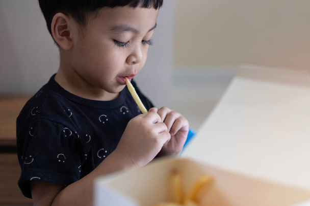 Retrato de un niño asiático pequeño y lindo comiendo papas fritas en la mesa en el restaurante o en casa de tres o cuatro años. - Foto, Imagen