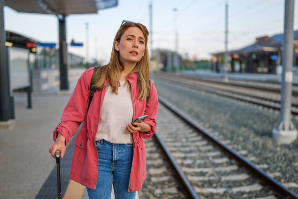 Felnőtt nő áll a vasútállomáson, és várja a vonat érkezését. - Fotó, kép