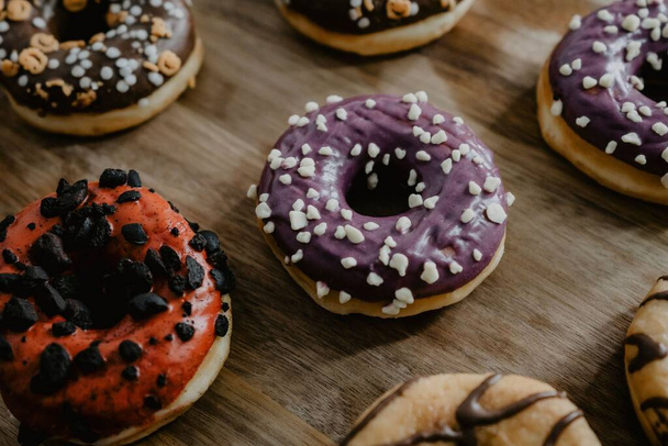 A closeup shot of freshly baked donuts, glazed with chocolate and vanilla, differently decorated, served on a wooden cutting board - Foto, imagen