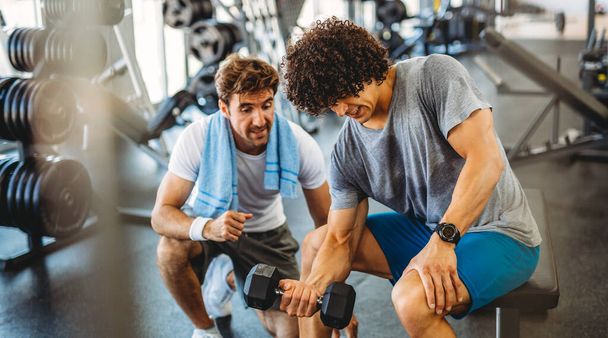 Fitness, sport, exercising and diet concept. Happy fit man exercising together with his personal trainer, friend in gym. - 写真・画像