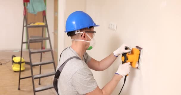 Erikoistunut kypärä ja suojaava hengityssuojain käsittelee seinään hiomakone. Professional laitteet kiillotus seinään asunnossa hidastettuna - Materiaali, video