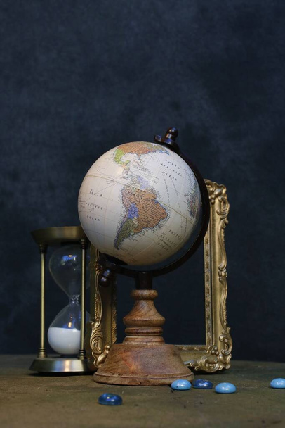 A vertical shot of a globe and hourglass on a dark background - Фото, зображення